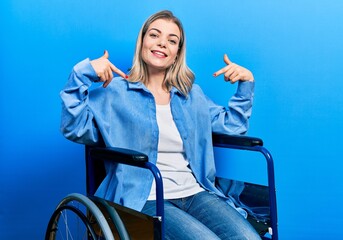 Beautiful caucasian woman sitting on wheelchair looking confident with smile on face, pointing...
