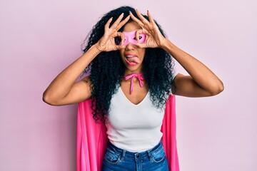 Middle age african american woman wearing super hero costume doing ok gesture like binoculars...