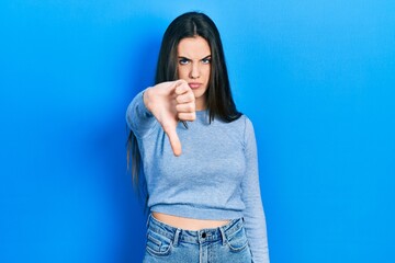 Young brunette teenager wearing casual sweater looking unhappy and angry showing rejection and negative with thumbs down gesture. bad expression.