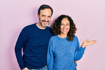 Obraz premium Middle age couple of hispanic woman and man hugging and standing together smiling cheerful presenting and pointing with palm of hand looking at the camera.