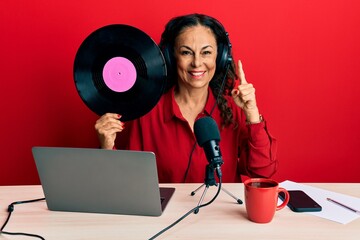 Beautiful middle age woman working at radio studio holding vinyl disc smiling with an idea or question pointing finger with happy face, number one