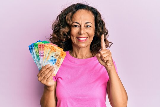 Middle age hispanic woman holding swiss franc banknotes smiling with an idea or question pointing finger with happy face, number one