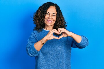 Middle age hispanic woman wearing casual clothes smiling in love doing heart symbol shape with hands. romantic concept.