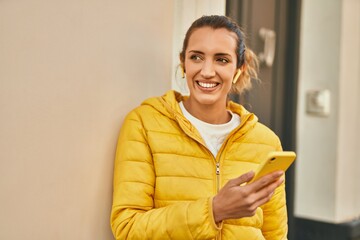 Young hispanic girl smiling happy using smartphone and earphones at the city.