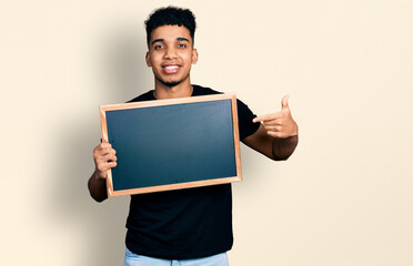 Young african american man holding blackboard smiling happy pointing with hand and finger