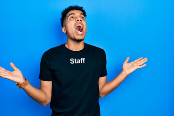 Young african american man wearing staff t shirt crazy and mad shouting and yelling with aggressive expression and arms raised. frustration concept.