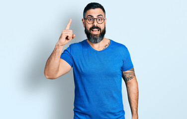 Hispanic man with beard wearing casual t shirt and glasses pointing finger up with successful idea. exited and happy. number one.