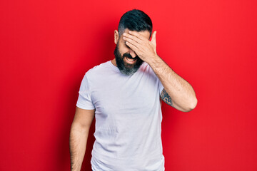 Young hispanic man wearing casual white t shirt surprised with hand on head for mistake, remember...