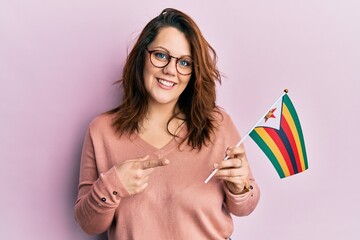 Young caucasian woman holding zimbabwe flag smiling happy pointing with hand and finger - obrazy, fototapety, plakaty