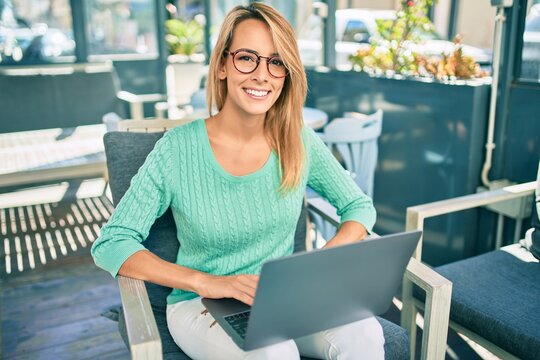 Young blonde woman smiling happy working using laptop sitting at the coffee shop terrace.