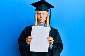 Beautiful blonde woman wearing graduation cap and ceremony robe holding blank banner depressed and worry for distress, crying angry and afraid. sad expression.
