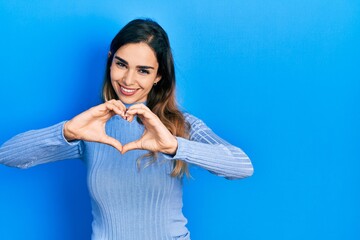 Young hispanic girl wearing casual clothes smiling in love doing heart symbol shape with hands. romantic concept.