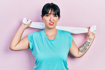 Young hispanic woman wearing sportswear holding towel clueless and confused expression. doubt...
