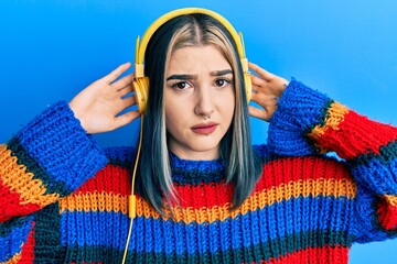 Young modern girl listening to music using headphones skeptic and nervous, frowning upset because...