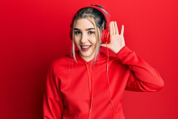 Young modern girl wearing gym clothes and using headphones smiling with hand over ear listening an hearing to rumor or gossip. deafness concept.