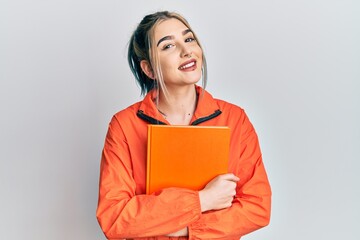 Young modern girl holding book smiling with a happy and cool smile on face. showing teeth.