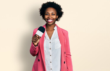 African american woman with afro hair holding reporter microphone looking positive and happy...