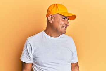 Mature middle east man with mustache wearing casual white tshirt and yellow cap looking to side, relax profile pose with natural face and confident smile.