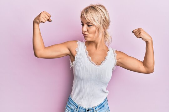 Young blonde girl wearing casual clothes showing arms muscles smiling proud. fitness concept.