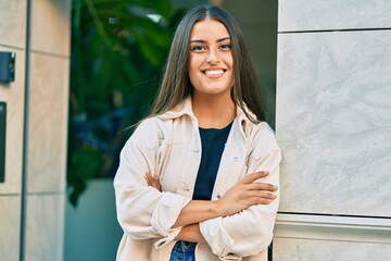 Young hispanic girl with crossed arms smiling happy at the city.