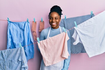 African american woman with braided hair washing clothes at clothesline winking looking at the...