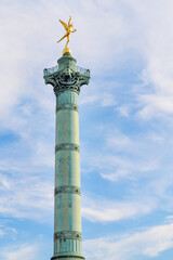 Side view of Colonne de Juillet, on the Place de la Bastille in Paris, France. Golden angel status on top and aa blue sky with many clouds.