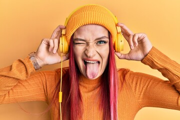 Young caucasian woman listening to music using headphones sticking tongue out happy with funny expression. © Krakenimages.com