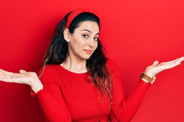 Young hispanic woman wearing casual clothes clueless and confused expression with arms and hands...