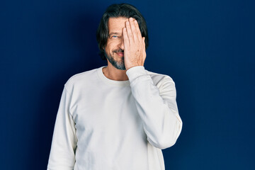 Middle age caucasian man wearing casual clothes covering one eye with hand, confident smile on face and surprise emotion.