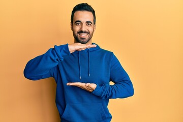 Young hispanic man wearing casual clothes gesturing with hands showing big and large size sign, measure symbol. smiling looking at the camera. measuring concept.