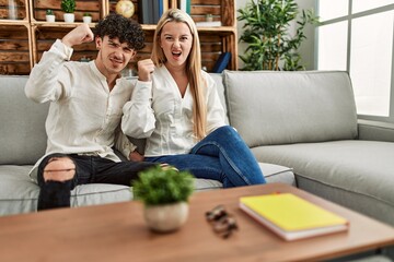 Young beautiful couple sitting on the sofa at home annoyed and frustrated shouting with anger, yelling crazy with anger and hand raised