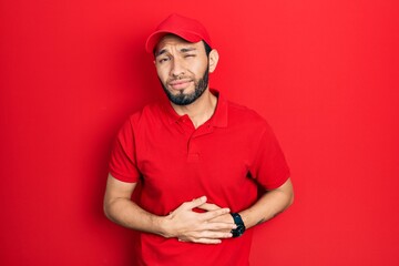 Hispanic man with beard wearing delivery uniform and cap with hand on stomach because indigestion, painful illness feeling unwell. ache concept.