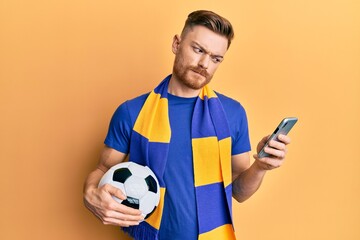 Young redhead man wearing hooligan scarf and using smartphone skeptic and nervous, frowning upset...