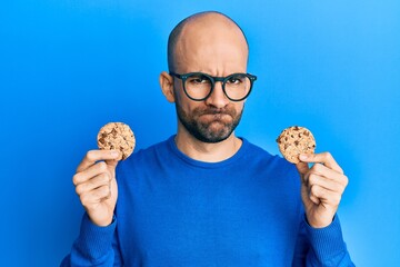 Young hispanic man holding chocolate chips cookies skeptic and nervous, frowning upset because of...