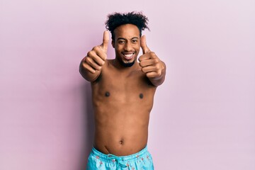 Fototapeta premium Young african american man with beard wearing swimsuit approving doing positive gesture with hand, thumbs up smiling and happy for success. winner gesture.