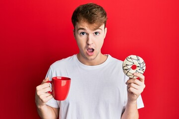 Young caucasian man drinking a cup of coffee and croissant afraid and shocked with surprise and amazed expression, fear and excited face.