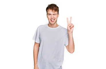 Fototapeta premium Young caucasian man wearing casual white t shirt smiling with happy face winking at the camera doing victory sign. number two.