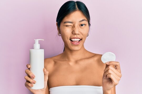 Young chinese woman wearing shower towel using clean lotion winking looking at the camera with sexy expression, cheerful and happy face.