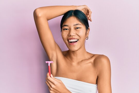 Young chinese woman wearing shower towel using razor smiling and laughing hard out loud because funny crazy joke.