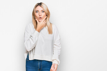 Young caucasian woman wearing casual winter sweater looking fascinated with disbelief, surprise and amazed expression with hands on chin