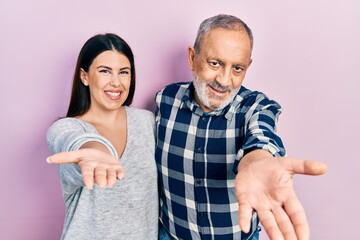 Hispanic father and daughter wearing casual clothes smiling cheerful offering palm hand giving assistance and acceptance.