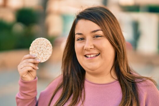 Young Hispanic Plus Size Woman Smiling Happy Eating Rice Cake At The City.