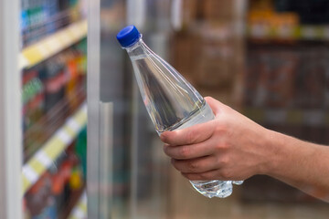 Man holds in his hand a plastic bottle with pure mineral water on the background of a shop window.