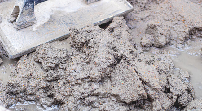 Cimento, Concreto. Carrinho de mão com mistura de cimento e areia e uma desempenadeira. Fotografia em close up. Obra, Construção, Reforma, objetos.