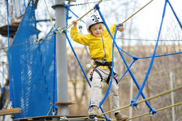 Little boy having fun in Adventure Park for children amoung ropes, stairs, bridges. Outdoor climbing adventure playground in public park. Activity entertainment for kids
