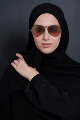 Young muslim businesswoman in traditional clothes or abaya and sunglasses posing in front of black chalkboard