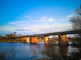 Fototapeta na wymiar Ancient bridge over the river with stone pillars. Rapid flow of water in spring. Sunset view.