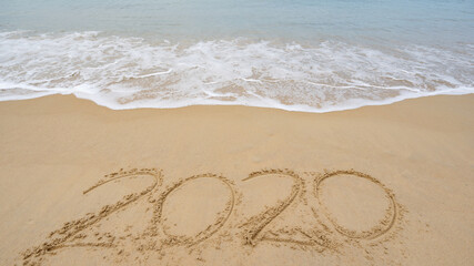 2020 Text on the beach, 2020 year message hand written in sand on beautiful beach Waves crashing on sandy shore background. New Years concept