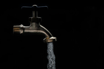 low key light of faucet witrh water flow in black back background