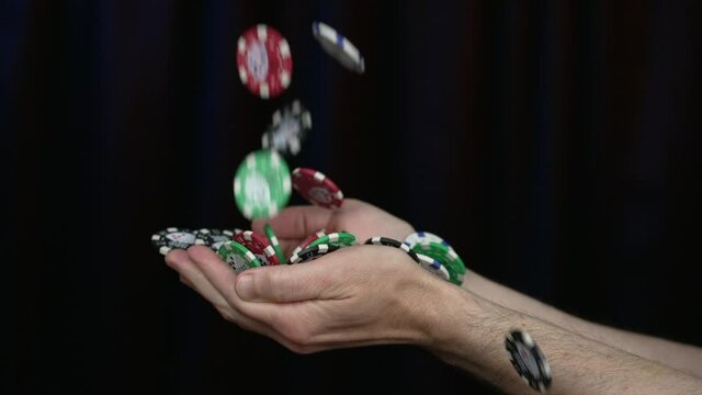 Casino gaming chips fall into a man's hands in slow motion. Shot at 120fps. Chips are generic and don't represent any particular casino. Black limbo background.  	